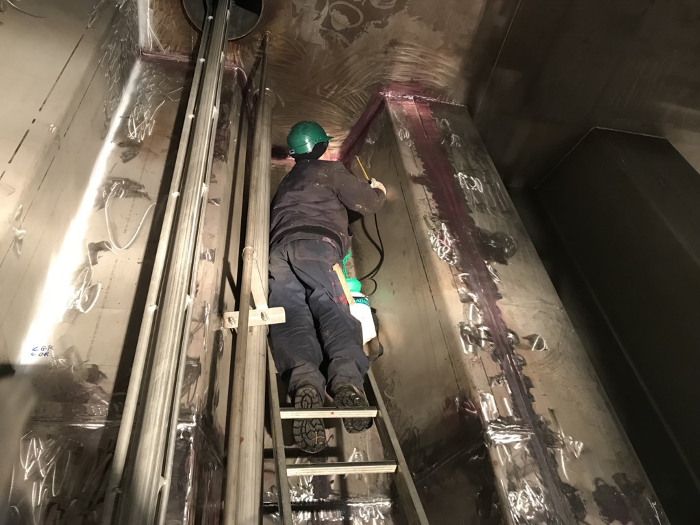 A person doing a welding job inside a stainless steel cargo tank