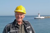 Man in black jacket and yellow helmet in front of lighthouse
