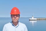 Man in blue shirt and red helmet in front of lighthouse