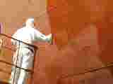 A person spray painting a ship side orange
