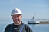 Man in black shirt and white helmet in front of lighthouse