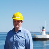 Man in blue shirt and yellow helmet in front of lighthouse