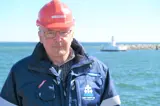 Man in blue jacket and red helmet in front of lighthouse