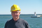 Man in black shirt and yellow helmet in front of lighthouse